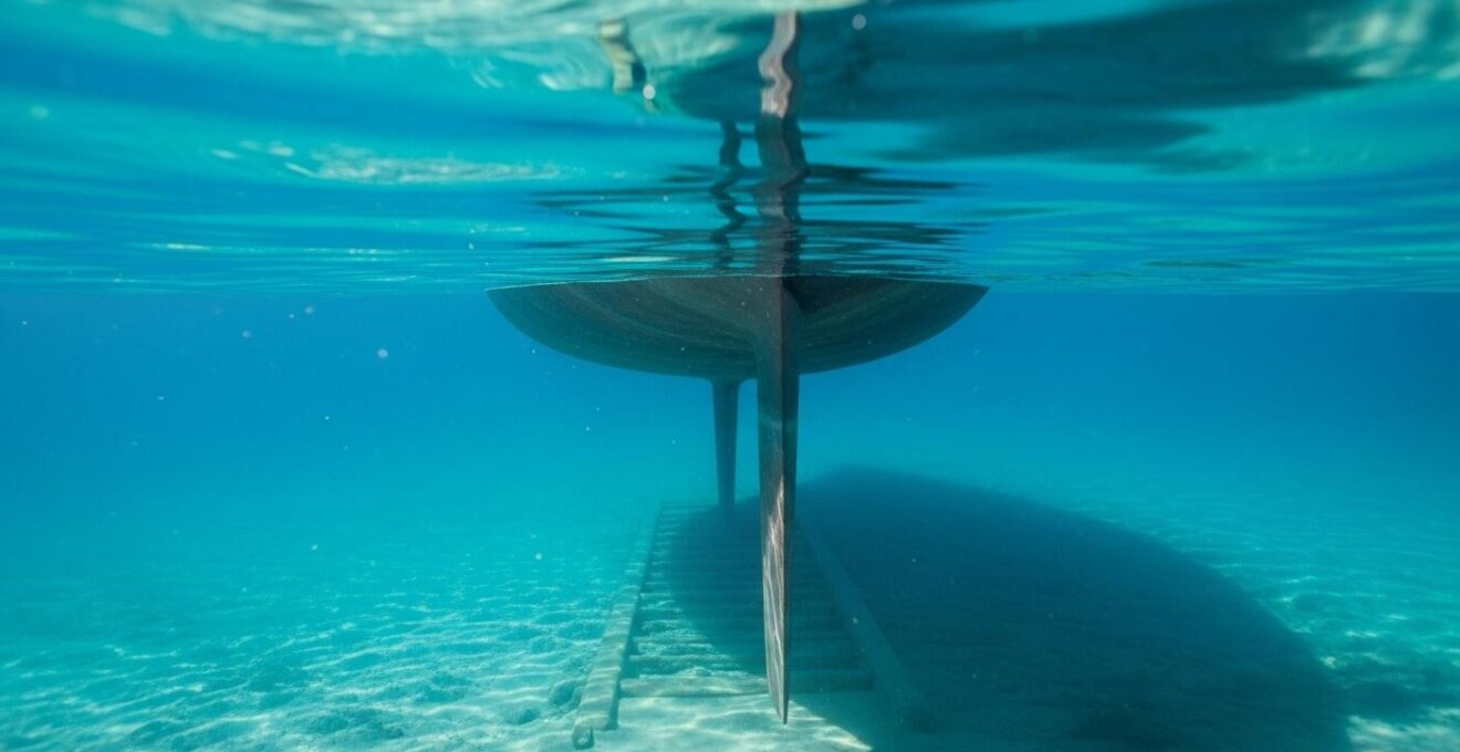 Voilier vu de côté avec la quille visible sous l'eau dans un mouillage marin pittoresque